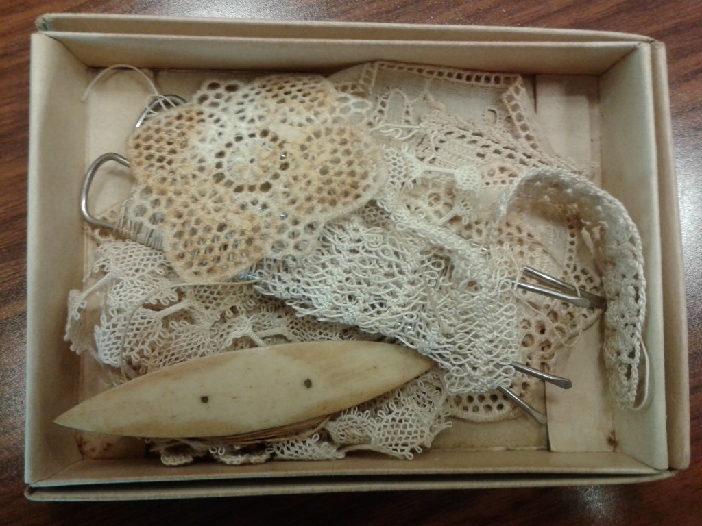 Inspecting an antique box of tatting with a shuttle made of ivory.